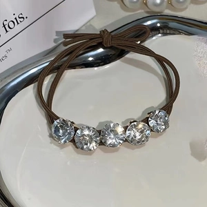 Close-up of brown elastic hair tie featuring five sparkling round rhinestones on a tray