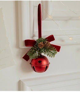 Detail of red velvet bow and metal bell with pine cones hanging on white wall