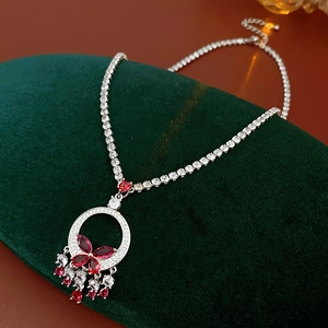 Detail of silver necklace with red butterfly pendant and tassels on green velvet