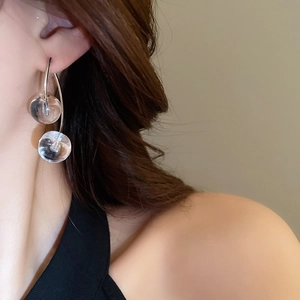 Close-up of minimalist silver cherry drop earrings featuring clear glass spheres on a model