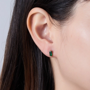 Close-up of a model wearing a minimalist gold stud earring with a green emerald-cut stone