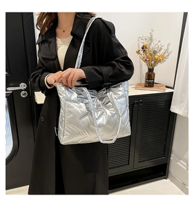 Detailed view of silver quilted tote bag on model showing glossy texture and strap detail