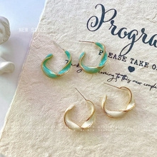 Macro shot of mint green and cream white C-shaped twisted enamel hoop earrings