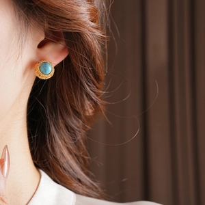 Close-up of vintage turquoise stud earring with embossed gold base on a female model