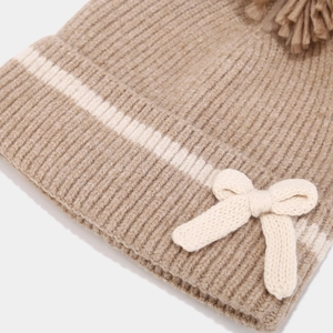 Detailed macro view of knit winter hat featuring brown stripes and a cream bow accent