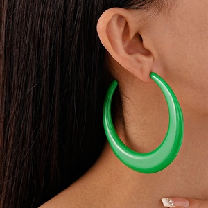 Close-up of oversized green acrylic hoop earrings featuring a bold C-shaped geometric design