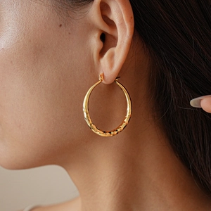 Detail of gold geometric textured hoop earring worn by a model showing large stylish design