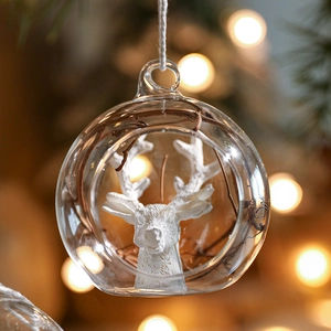 Clear glass Christmas ornament with white reindeer relief and wood branch inside on warm tree