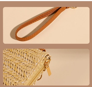 Detail of straw woven purse featuring a brown leather wrist strap and gold metal zipper