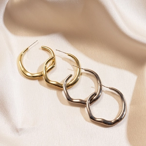 Irregular wave geometric hoop earrings in gold and silver finish on silk background