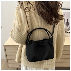 Detail view of a black bucket bag styled with a beige knit sweater for daily commute