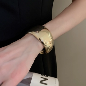 Gros plan d'un large bracelet jonc minimaliste plaqué or avec une finition miroir polie