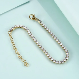 Detail of gold tennis bracelet with clear round stones and lobster clasp on teal background