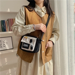 Detail view of a beige and black canvas crossbody bag with buckle and badges on a model