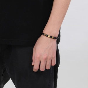 Black beaded bracelet with gold accents on male wrist against a clean white wall