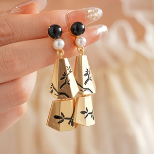Detailed close-up of gold tassel earrings with pearls and black leaf patterns