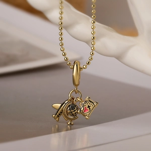 Gold beaded necklace with airplane and globe travel charms on neutral background