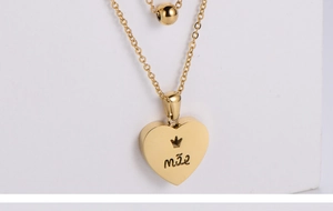 Detail of gold titanium steel heart pendant with mae engraving and double layered chain