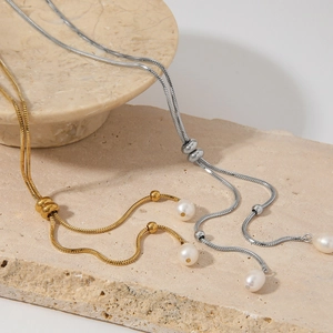 Elegant gold and silver Y-shaped snake chain necklaces with natural pearls on stone pedestal