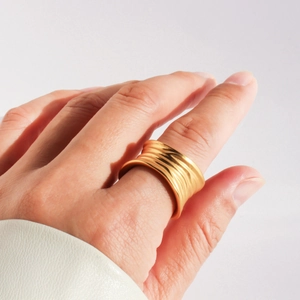 Detailed close-up of wide gold ring with irregular handcrafted texture on model finger