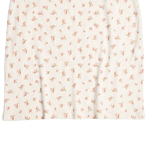 Detailed macro view of white ribbed knit fabric with red floral patterns on the dress hem