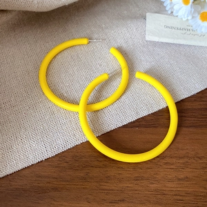 Macro shot of matte yellow leaf-shaped drop earrings on soft fabric with daisies