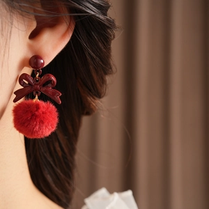 Detail of model wearing wine red bow earrings with red plush pompom on silver needle