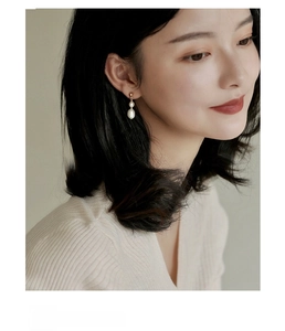 Close-up of elegant freshwater pearl dangle earrings on model with golden metal hooks