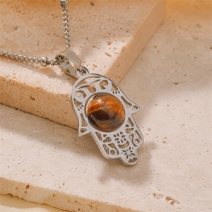Silver stainless steel Hamsa Hand pendant necklace with tiger eye stone on stone background