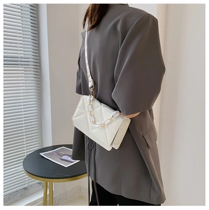 White quilted crossbody bag with a wide letter-print strap shown on a model in a modern room