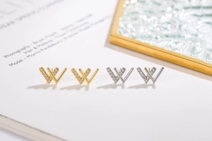 Detailed close-up of gold and silver double W-shaped earrings with zircon inlays