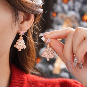 Detail view of crystal-encrusted Christmas tree earrings with pink star on a model