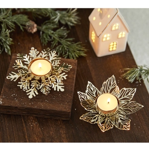 Détail de bougeoirs en fer doré avec motifs flocons et feuilles sur table en bois