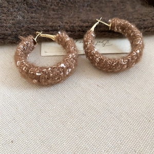 Makroaufnahme von gestrickten Creolen aus dunkelbraunem Garn mit goldenen Metalldetails