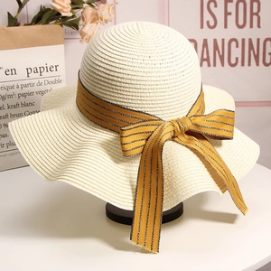Detail of a beige woven straw sun hat with a decorative yellow striped ribbon bow