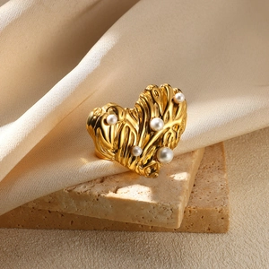 Detailed view of a gold heart ring with irregular texture and pearls on beige stone
