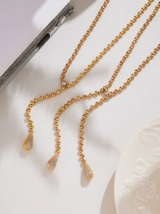 Détail d'un collier chaîne à billes doré avec des pendentifs gouttes en zircone