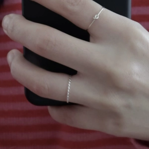 Detailed view of simple silver knot ring and slim band on finger with phone