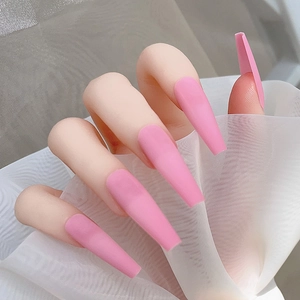 Détails de faux ongles ballerine longs rose mat posés sur un tissu en maille blanche douce