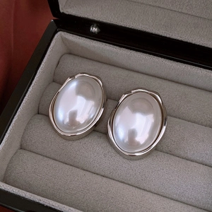 Macro detail of oval white pearl earrings with irregular silver metal frames in a gift box