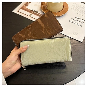 Detail of coffee and green long zip wallets with pleated texture held by hand