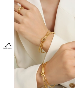 Detail of golden knotted heart bracelet and ring set on model in white blazer