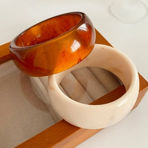 Close-up of thick resin bangles in amber and cream white on a wooden jewelry display box