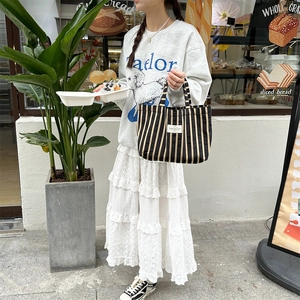 Detail of a large capacity striped canvas tote bag with a white woven label on the front