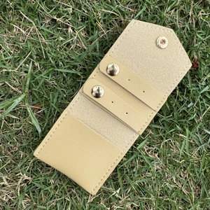 Detail view of beige leather jewelry pouch with snap button and straps on grass