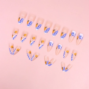 Close-up of almond-shaped press-on nails with white leaf and orange fruit patterns