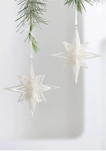 Close-up of white glitter star ornaments hanging on green pine branches for Christmas decor