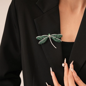 Elegant dragonfly brooch with green gemstones and silver base on black suit lapel