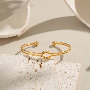 Detail shot of a minimalist gold-plated knot cuff bracelet on a natural stone base