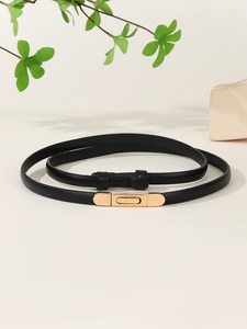 Detail of slim black patent leather belt with a rectangular gold buckle and metal clasp